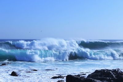 Scenic view of waves rushing towards shore against clear sky