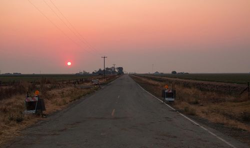 Road amidst field against clear sky during sunset