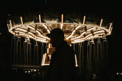 Side view of silhouette man against illuminated amusement park ride