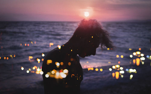 Double exposure image of silhouette man at beach and illuminated cityscape