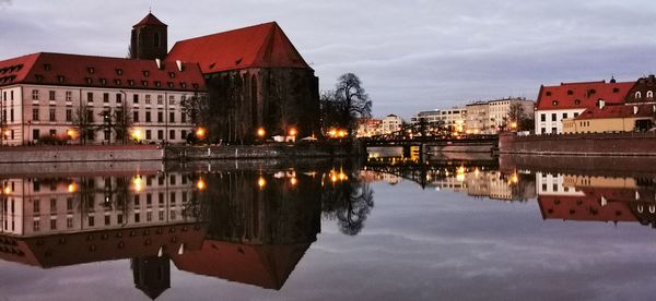 Reflection of buildings in lake against sky in city at dusk