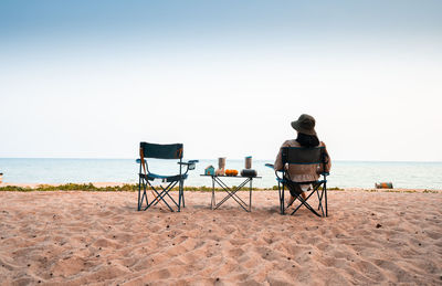 Asian female tourists sit on beach chairs, tables with orange speakers, glasses, and house models.