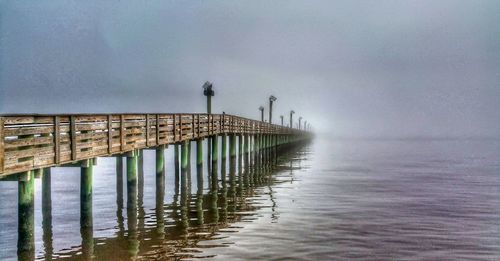 Bird perching on pier over sea against sky