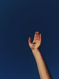Cropped hand against clear blue sky