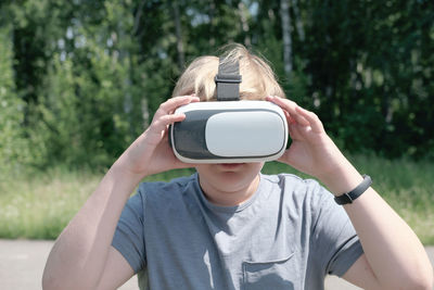 Blond teenager boy using vr headset for playing outdoors. teen boy touching a virtual reality gadget