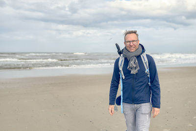 Smiling man standing on sea shore at beach against cloudy sky