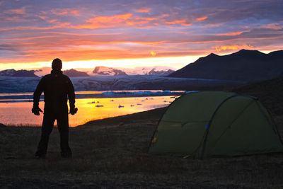 Silhouette man standing at campsite against cloudy sky during sunset