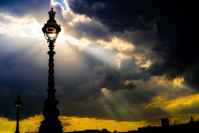 Low angle view of silhouette gas light against dramatic sky