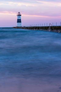 Lighthouse by sea against sky during sunset