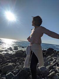 Man standing on rock by sea against sky on sunny day