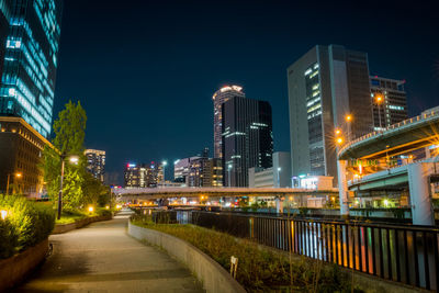Illuminated street by buildings against sky at night