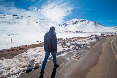 Rear view of man walking on road by snow covered mountains