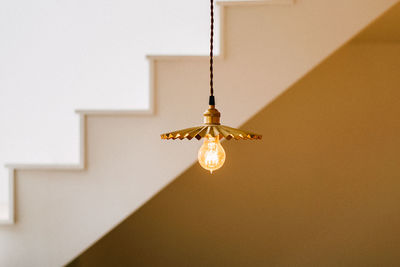 Low angle view of illuminated light bulb hanging from ceiling