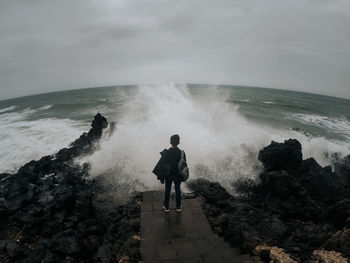 Rear view of man standing on rock against sea