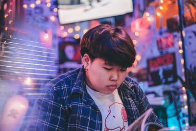 Young woman reading book against illuminated lighting equipment