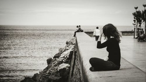 Side view of woman sitting on retaining wall