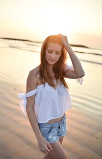 Beautiful young woman standing on beach against sky