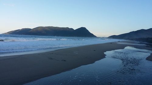 Scenic view of sea and mountains against clear blue sky