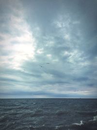 Birds flying over sea against cloudy sky