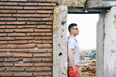 Side view of young man standing against brick wall