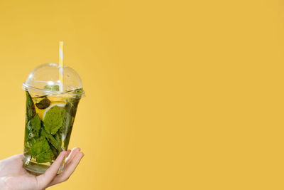 Close-up of hand holding drink against yellow background