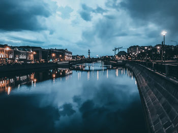 Bridge over river by buildings against sky at dusk