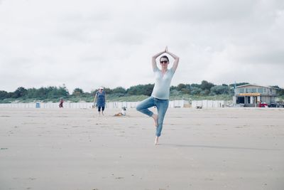 Full length of woman performing yoga at beach against sky