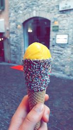 Cropped hand of person holding ice cream cone against building