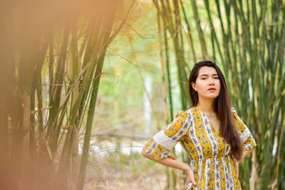 Young woman looking away while standing against plants