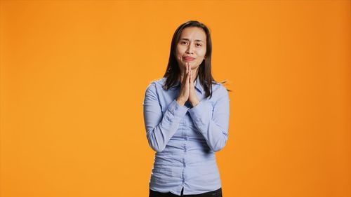 Portrait of young woman standing against yellow wall