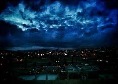 Illuminated cityscape against cloudy sky