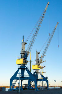 Cranes at commercial dock against clear blue sky