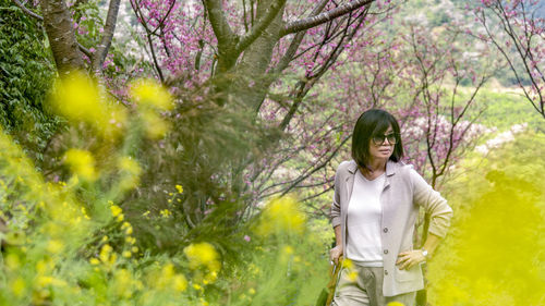 Woman standing by flowering plants against trees