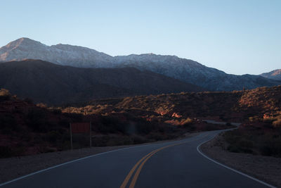 Road leading towards mountains against clear sky