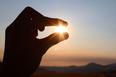 Close-up of hand holding sun against sky during sunset