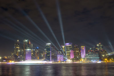 Illuminated buildings by river against sky at night