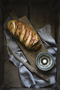 Artisan loaf of bread on board with knife, blue patterned bowl, linen