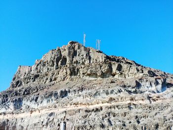 Low angle view of rocky mountain against clear blue sky