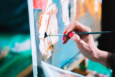 Close-up of woman hand painting on canvas in studio