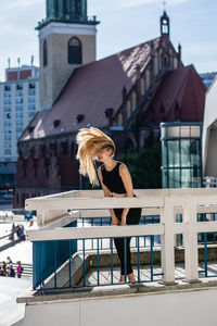 Playful young woman tossing hair on balcony against buildings in city