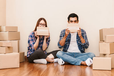 Portrait of couple with cardboard boxes sitting on floor at new home