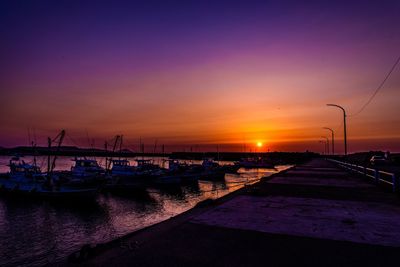Boats moored at harbor against sky during sunset
