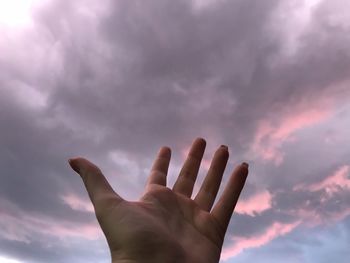 Low angle view of person hand pleading while praying against sky