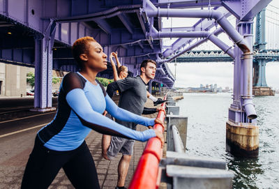 People exercising while standing by railing on bridge over river in city