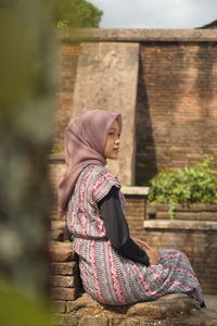 Side view of young woman sitting on wall