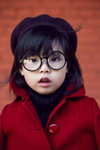 Korean girl in a red coat and cap and round glasses stands on red brick wall the street in autumn.