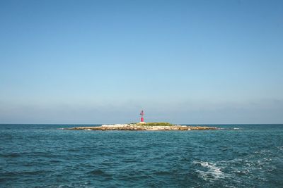 Lighthouse by sea against clear sky