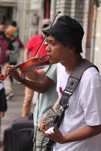 Young man playing guitar on the sidewalk in city