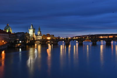 Illuminated buildings by river against sky in city