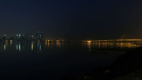 Illuminated city by lake against clear sky at night